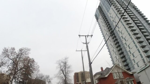 2-2 POV upward steady motion view of car driving past vintage residential homes apartments townhomes attached housing on a fall day with bare trees headed to a post modern futuristic resident tower
