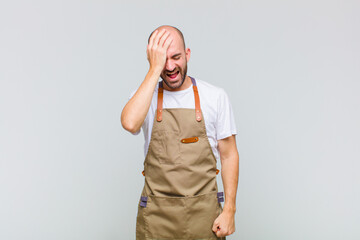 bald man laughing and slapping forehead like saying d’oh! I forgot or that was a stupid mistake