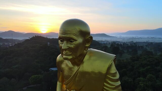 4k Aerial Close up shot of a Biggest Luang Pu Thuat statue in the world surrounded by mountains of Khao Yai at dawn in Thailand. Panning right to left around Image of man made of gold. Medium shot