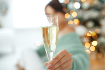 Smiling woman with glass of sparkling wine under Christmas tree lights background. High quality photo