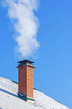 On a windless frosty winter day white smoke rises from the chimney against the blue sky