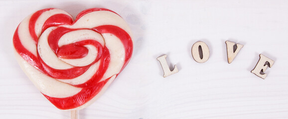 Inscription love and sweet lollipop in shape of heart as surprise for birthday, valentine or different occasions