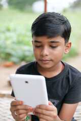 Indian little boy using digital tablet while attending the online classes at home with nature outside environment	
