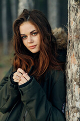 pretty red-haired woman in warm jacket near tree in nature forest