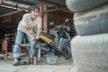 The tire patcher smiles looking at the camera while preparing a traditional press before patching the inner tube in a motorcycle repair shop
