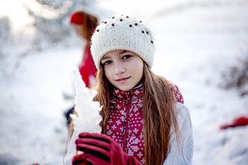 Happy girl playing with snow in frosty winter . Child dressed white hat , red vest and white blouse, walking in the snowy nature and tastes the icicle