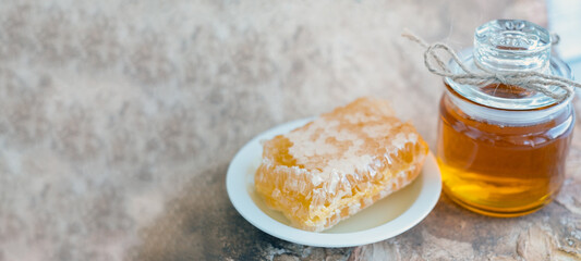 glass jar full of honey, plate with honeycomb on light brown background