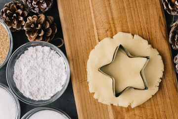Cutting Holiday Star Cookie In Raw Cookie Dough With Pine Cones And Ingredients on Slate