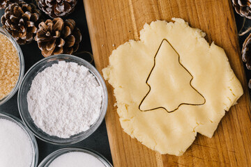 Cutting Holiday Christmas Tree Cookie In Raw Cookie Dough With Pine Cones And Ingredients on Slate
