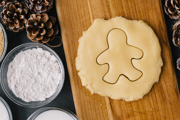 Cutting Christmas Ginger Bread Man Cookie In Raw Cookie Dough With Pine Cones And Ingredients on Slate