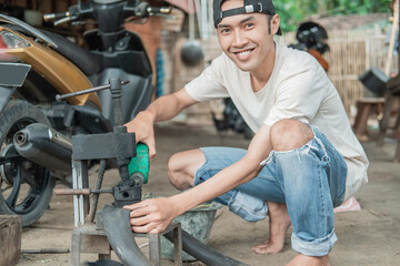 Tire repairman smiles at the camera while pouring fuel on a traditional press while patching tires in a repair shop