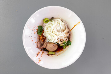 Thai noodle dry vermicelli with porks in tiny white bowl on grey rustic table.