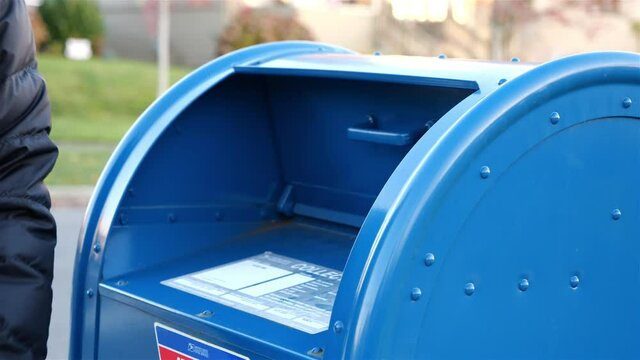 Woman drops a letter into a blue USPS mail box