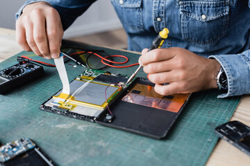 Close up view of hands of repairman with flex cable and screwdriver near disassembled digital...