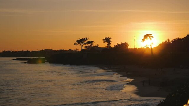 People at dog beach in Santa Cruz California with orange sunset sky at dusk, Pan right slow reveal shot