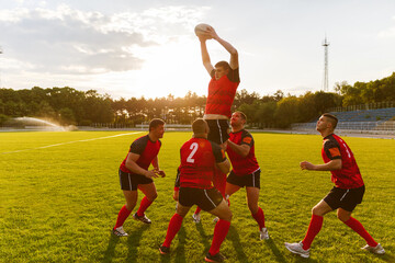 Full length image of a group of men in sports equipment play rugby on a sports field outside.