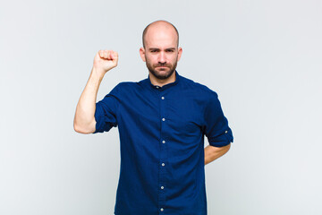 bald man feeling serious, strong and rebellious, raising fist up, protesting or fighting for...