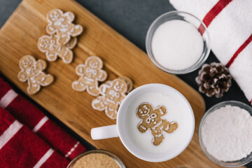 Fototapeta na wymiar Christmas Holiday Ginger Bread Man Cookie Floating In Mug Of Milk With Cookies And Baking Material