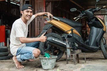 Fototapeta na wymiar Tire repair shop smiles with thumbs up when finished to repair a damaged motorcycle tire with traditional tools in the workshop