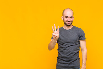 bald man smiling and looking friendly, showing number three or third with hand forward, counting...