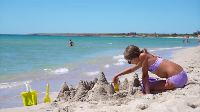 Little girl at tropical white beach making sand castle