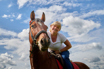 Obraz premium Girl riding on a horse on a green field and a blue sky with white clouds on the background