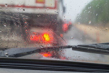 View of the road from the rain-drenched windshield of the car. Red light from the headlights ahead of Manina standing in the rain.