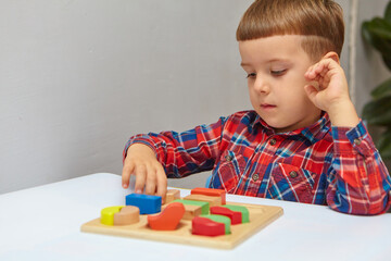 The boy is playing in his room. Learning shapes and colors. A child plays with a sorter. Educational logic toys for kid's. Montessori Games for Child Development.