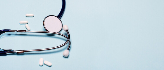 Stethoscope and white pills on a light blue background. Place to insert text or illustrations....