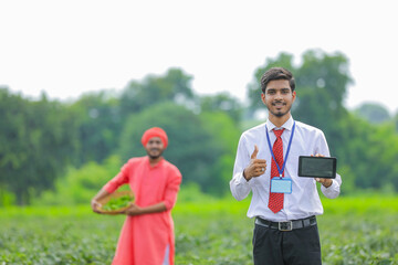 Young indian agronomist showing smart phone with farmer at green chilly field