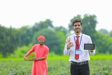 Naklejka premium Young indian agronomist showing smart phone with farmer at green chilly field