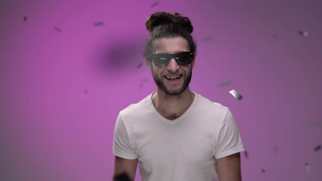 shiny confetti falls from above on pink background on a brutal guy with brody in white t-shirt and black glasses. He dances and enjoys celebration and magic High quality FullHD footage
