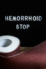 Words Hemorrhoids Stop and a roll of toilet paper wrapped in sandpaper.