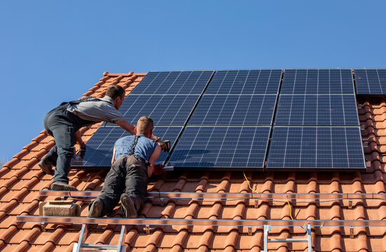 Workers installing solar electric panels on a house roof in  Ochojno. Poland