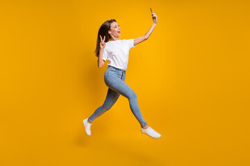 Fototapeta na wymiar Full length body size photo of female influencer taking selfie showing v-sign isolated on vibrant yellow color background