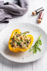 Stuffed sweet peppers with rice mushrooms and cheese with herbs. Baked halves of yellow peppers with filling. White wooden background.