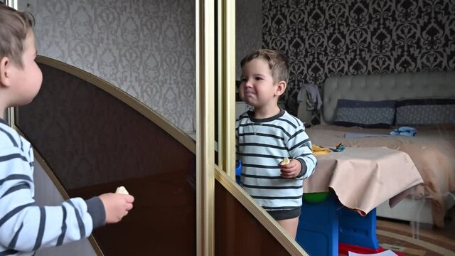 Cute little funny boy posing in front of mirror indoors. Toddler boy holding a slice of banana and jumping