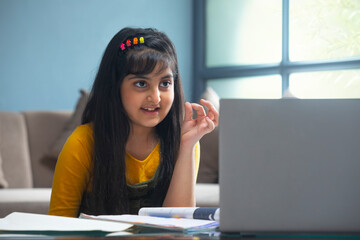 Young girl calculating numbers on her fingertips in front of her laptop during online class	