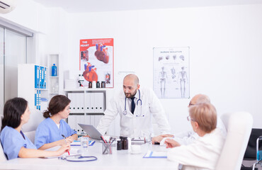 Young medical specialist discussing about patient diagnosis with coworkers in hospital conference room. Clinic expert therapist talking with colleagues about disease, medicine professional