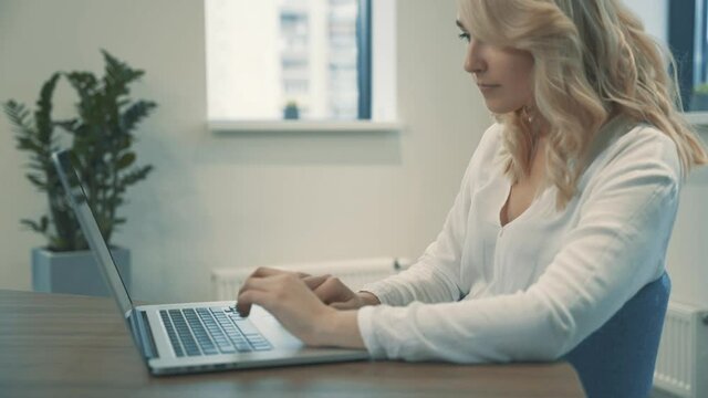 Pretty young blonde woman working from home typing with laptop