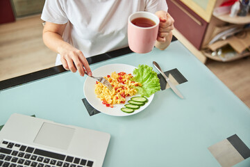 Female poking an omelet with a fork while having tea