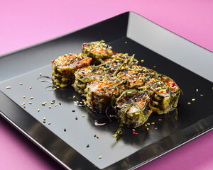 Sushi set served on a black square plate over bright pink background. Traditional Japanese cuisine, sushi rolls close up