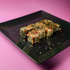 Sushi set served on a black square plate over bright pink background. Traditional Japanese cuisine, sushi rolls close up