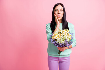 Photo portrait of shocked woman holding flowers in hands touching face cheek isolated on pastel pink colored background with blank space