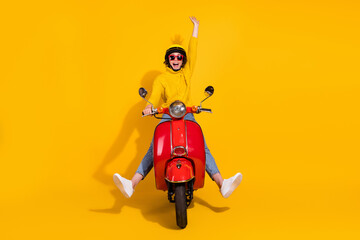 Photo portrait of cheerful girl raising one hand up riding red retro moped isolated on vivid yellow colored background