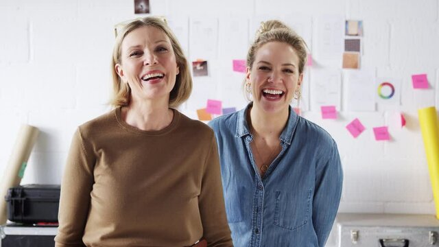 Portrait of two laughing women running creative business in studio together smiling at camera - shot in slow motion