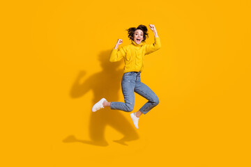 Fototapeta na wymiar Full length body size photo of jumping high girl gesturing like winner in warm sweater isolated on vibrant yellow color background