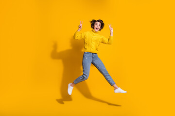 Fototapeta na wymiar Full length body size photo of jumping high girl showing v-sign peace with both hands isolated on bright yellow color background