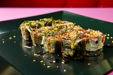 Sushi set served on a black square plate over bright pink background. Traditional Japanese cuisine, sushi rolls close up