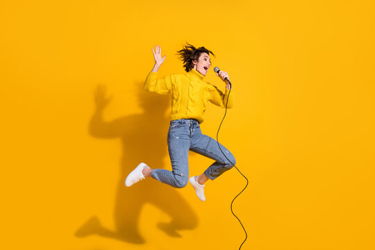 Full length body size photo of jumping female pop star singing in microphone on concert isolated on vibrant yellow color background